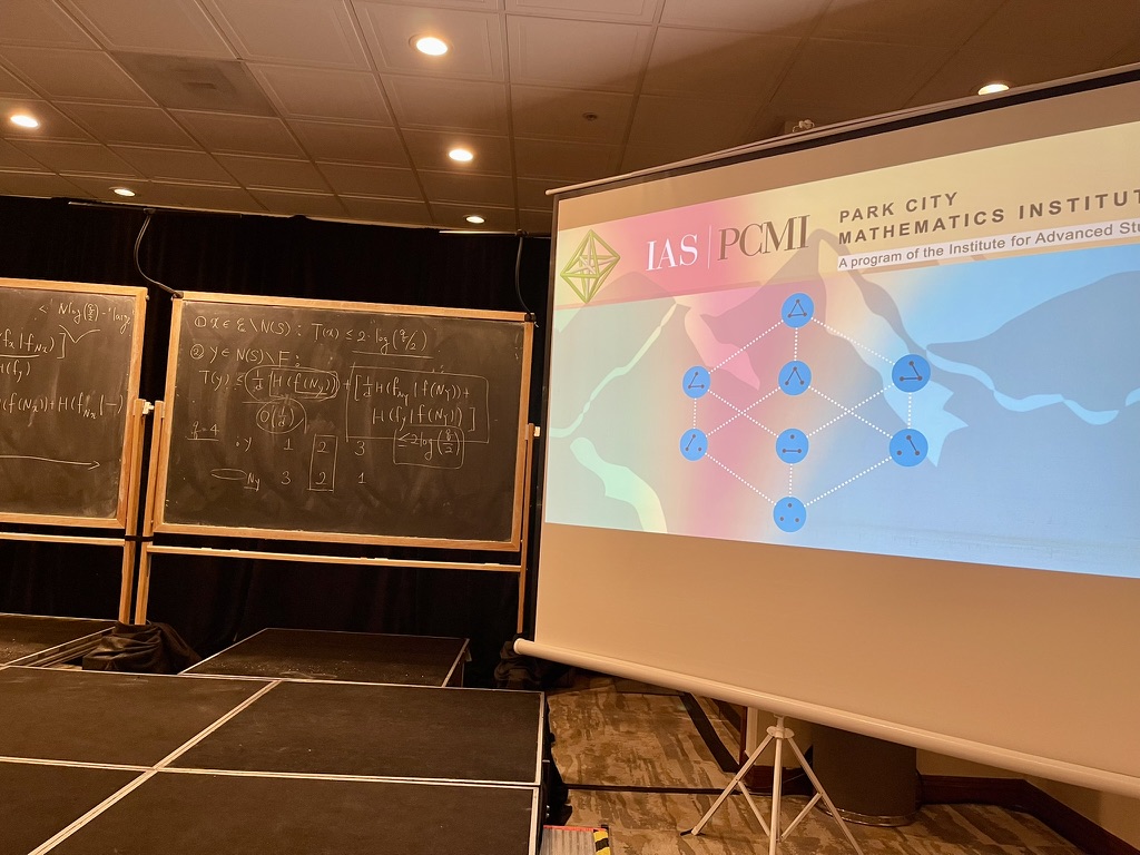 A title slide reading IAS PCMI Park City Mathematics Institute, a program of the Institute for Advanced Study, next to blackboards covered in notes from a lecture.