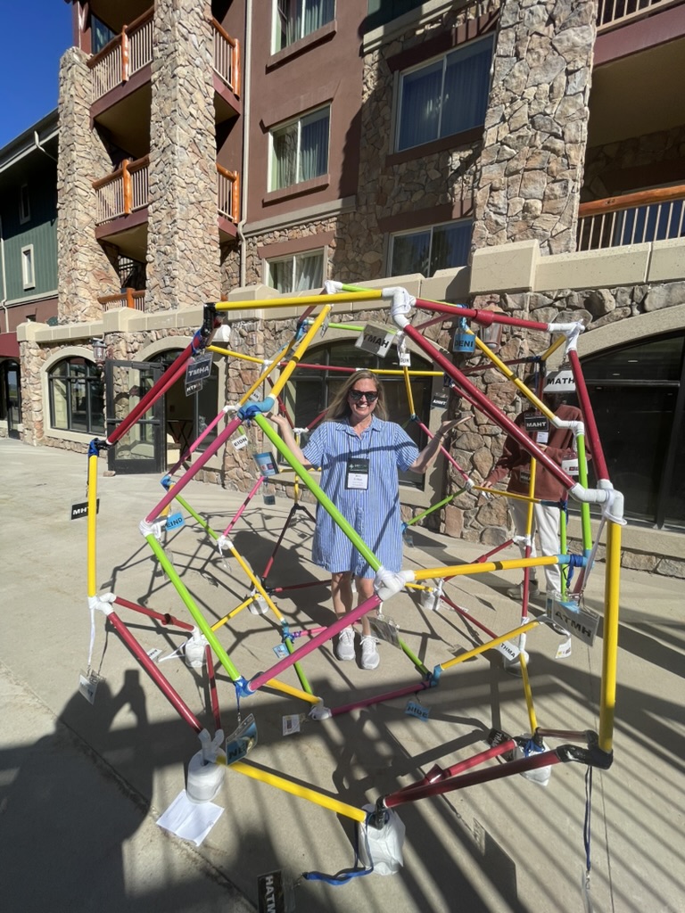 Ann standing inside a large colorful geometric sculpture made of connected rods, in front of a building at Park City.