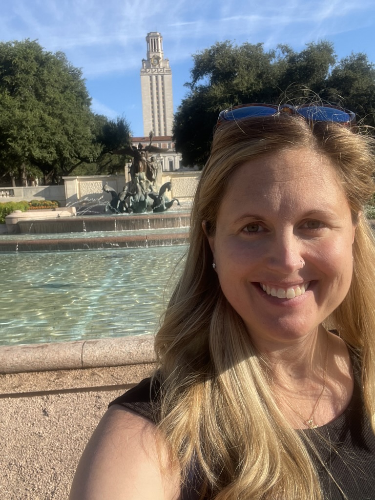 Ann smiling in front of the UT Austin Tower and the Littlefield Fountain.